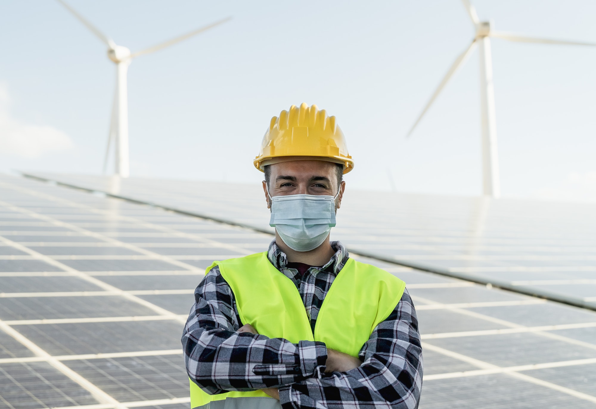 Young engineer working for alternative energy with wind turbine and solar panel while wearing mask